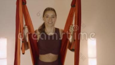 在瑜伽室吊床上荡秋千的女人。坐在吊床上做空中瑜伽的女孩